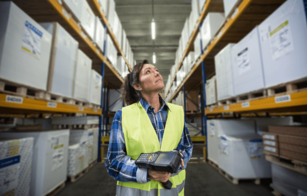 Person wearing a safety vest holding a barcode scanner inside of a wearhouse