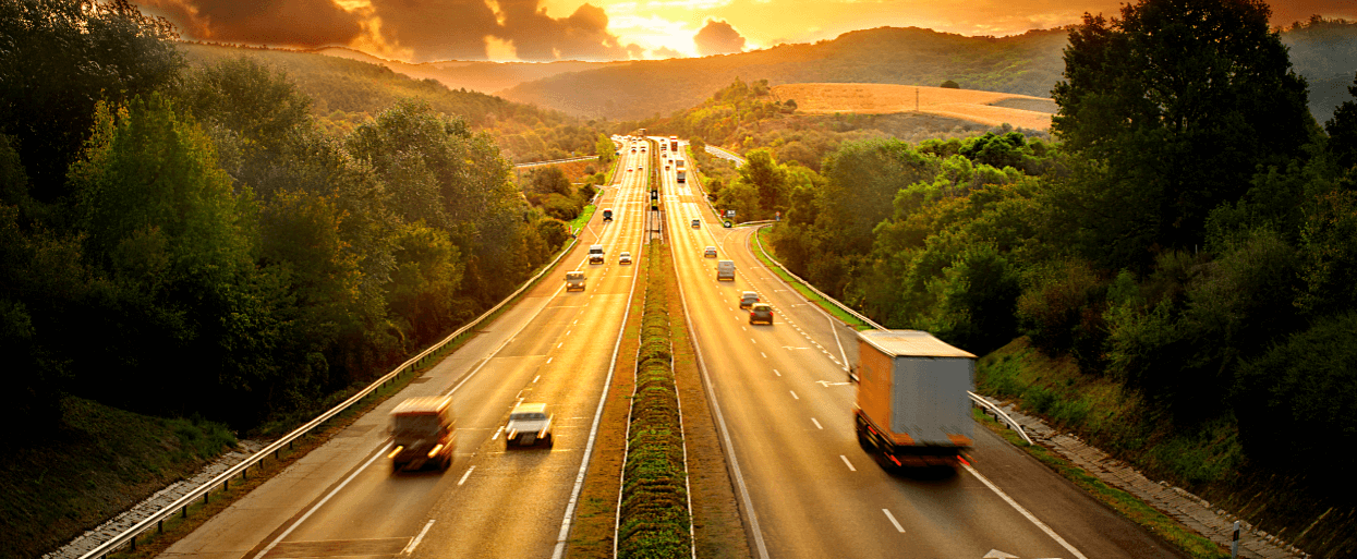 Six lane highway with split divider and vehicles traveling on both sides at sun set